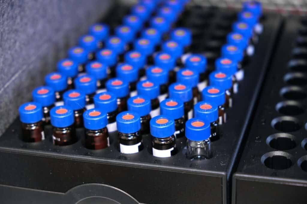 Glass vials with blue caps are in the rack of HPLC system with autosampler. Separation of compounds