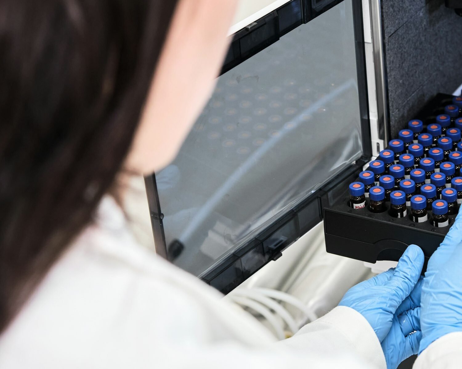 Scientist in a white lab coat putting vial with a sample into autosampler of HPLC system. High