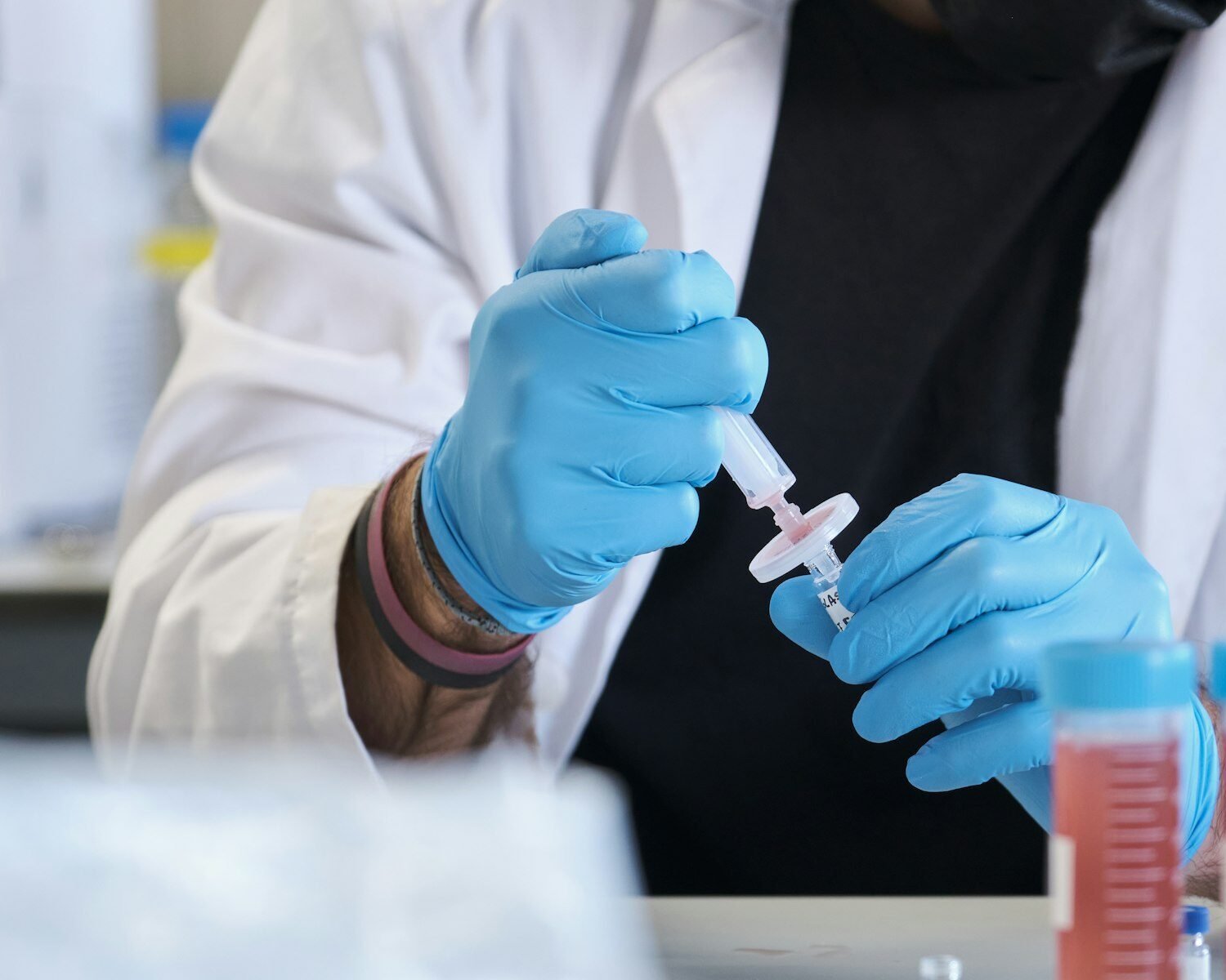 Scientist in white lab coat filter sample into HPLC vial.