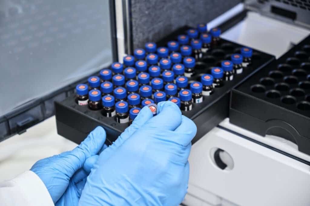 Chemist putting vial with a sample into autosampler of HPLC system. High performance liquid