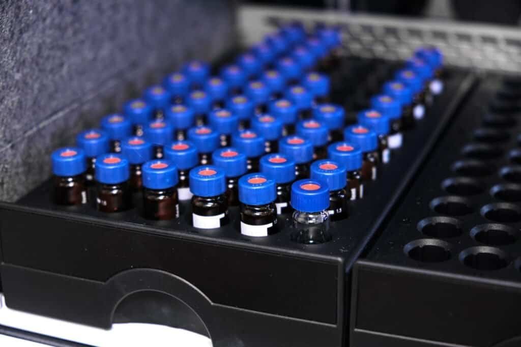 Glass vials with blue caps are in the rack of HPLC system with autosampler. Separation of compounds