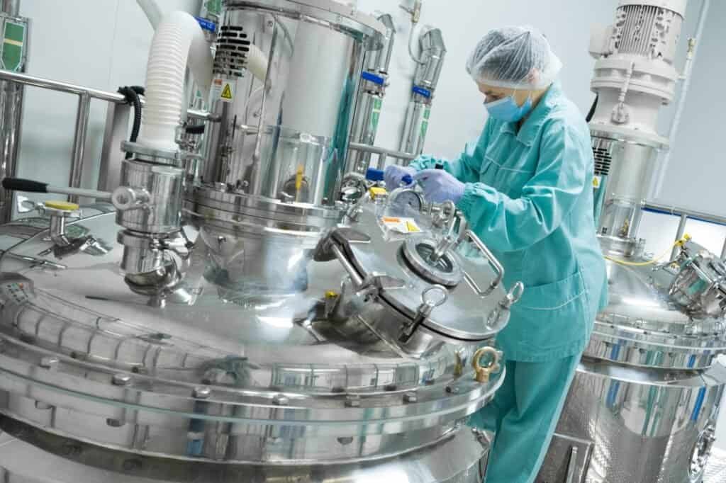 Pharmaceutical factory woman worker in protective clothing operating production line in sterile