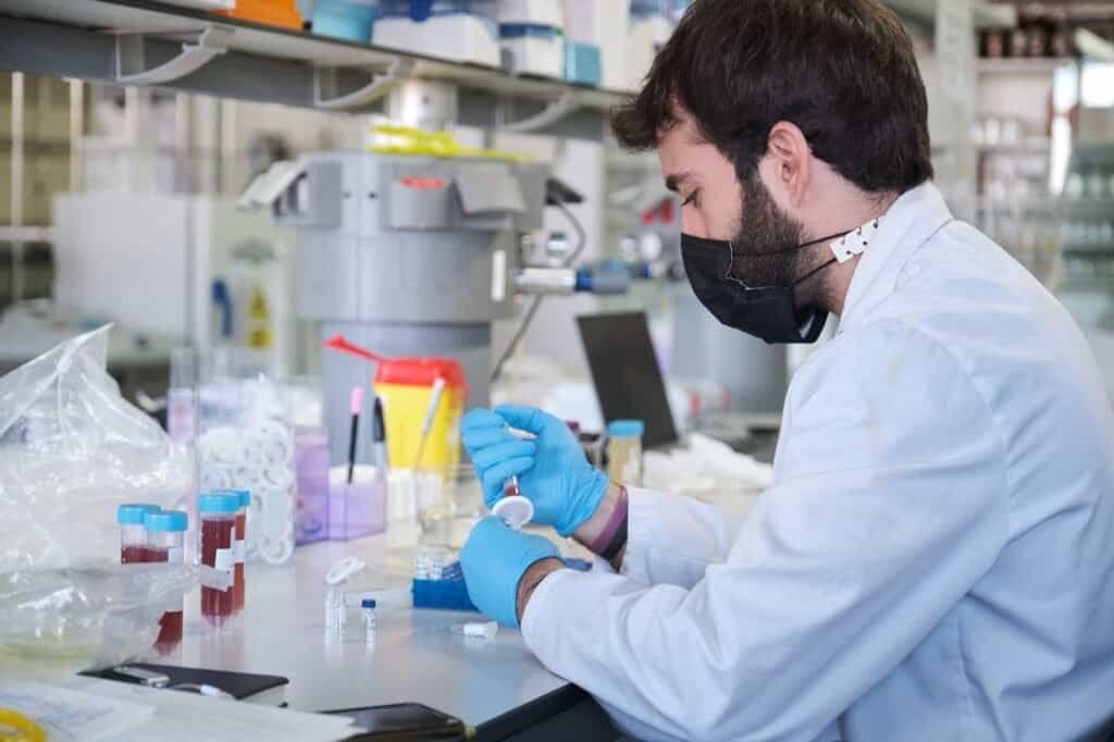 Scientist in white lab coat and face mask filter sample into HPLC vial.