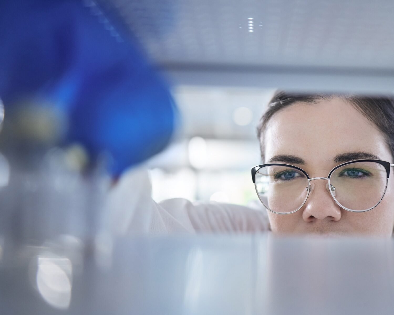 Closeup of unknown caucasian medical scientist wearing glasses and looking at a medicine vial in a