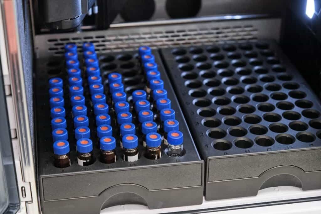 Glass vials with blue caps are in the rack of HPLC system with autosampler. Separation of compounds