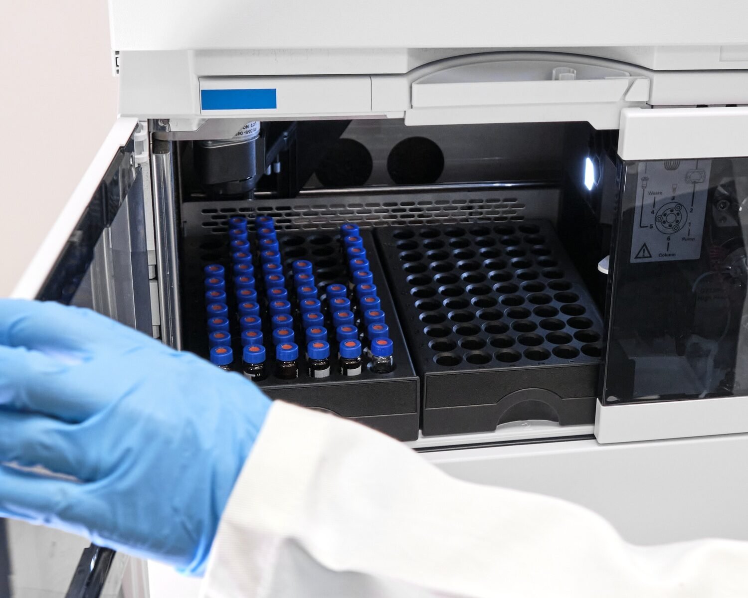 Scientist in a white lab coat putting vial with a sample into autosampler of HPLC system. High