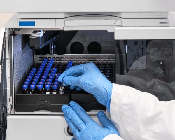 Scientist in a white lab coat putting vial with a sample into autosampler of HPLC system. High