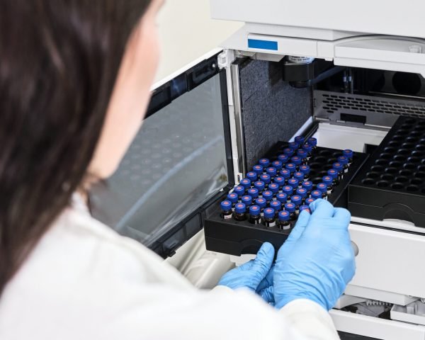 Scientist in a white lab coat putting vial with a sample into autosampler of HPLC system. High